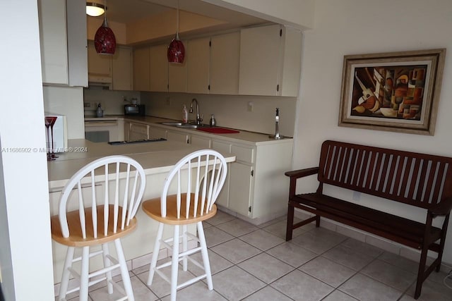 kitchen with white electric range oven, kitchen peninsula, sink, light tile patterned floors, and a kitchen breakfast bar