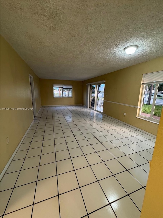 tiled empty room with a textured ceiling and a healthy amount of sunlight