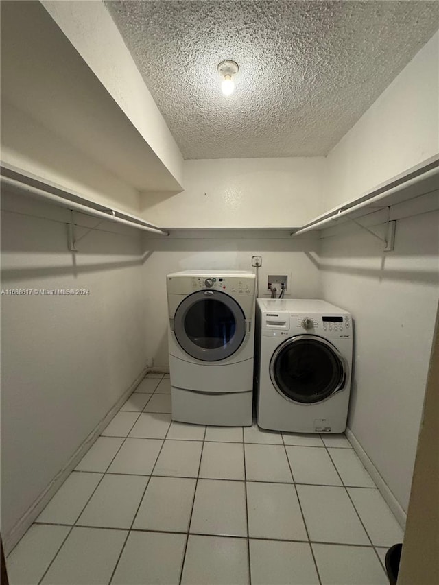 clothes washing area with independent washer and dryer, light tile patterned floors, and a textured ceiling