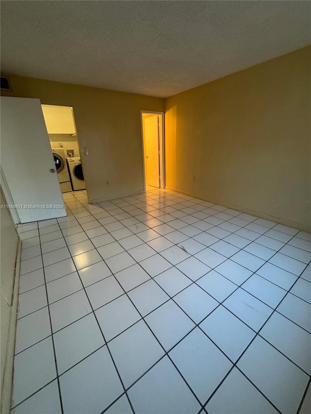 unfurnished room featuring a textured ceiling, light tile patterned floors, and washing machine and clothes dryer