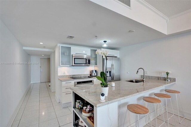 kitchen featuring white cabinets, sink, ornamental molding, a breakfast bar, and appliances with stainless steel finishes