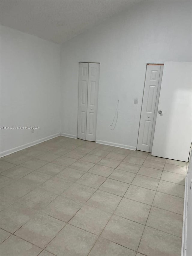 spare room with lofted ceiling, a textured ceiling, and light tile patterned flooring