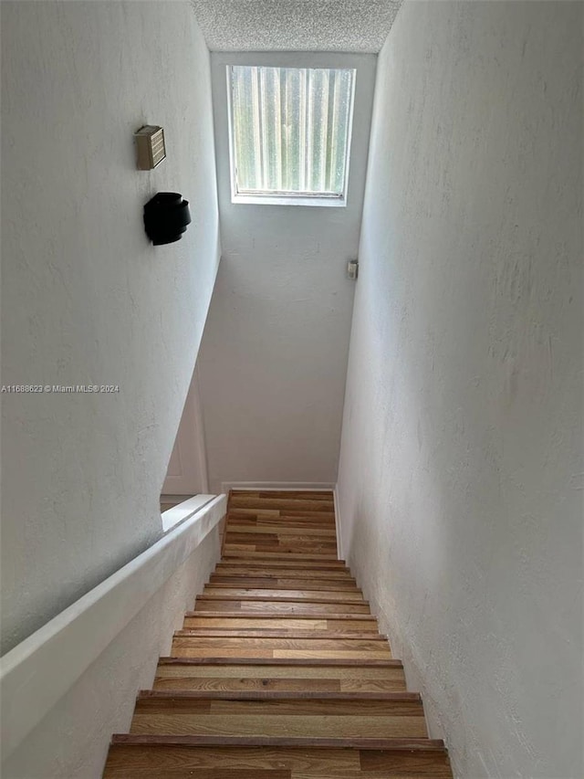 stairway with hardwood / wood-style floors and a textured ceiling