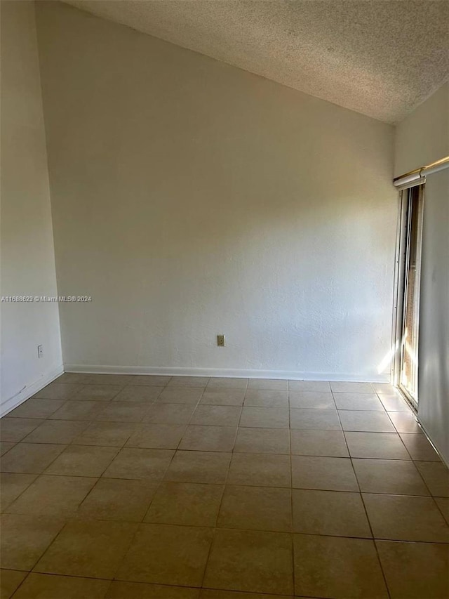 empty room with a textured ceiling, vaulted ceiling, and light tile patterned floors