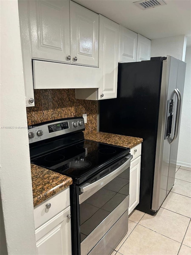 kitchen featuring decorative backsplash, light tile patterned flooring, electric range, white cabinetry, and dark stone countertops