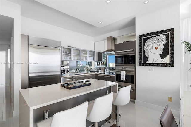 kitchen featuring a kitchen bar, wall chimney exhaust hood, a kitchen island, appliances with stainless steel finishes, and built in desk