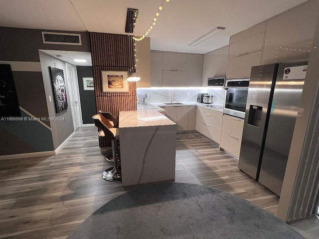 kitchen featuring wood-type flooring, sink, a breakfast bar, white cabinetry, and appliances with stainless steel finishes