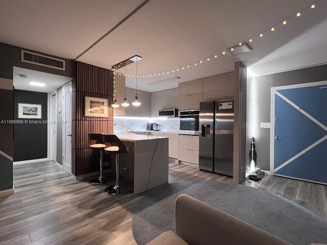 kitchen with appliances with stainless steel finishes, pendant lighting, hardwood / wood-style floors, a kitchen breakfast bar, and white cabinets