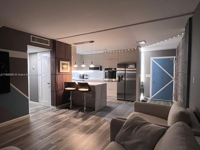 kitchen featuring hanging light fixtures, hardwood / wood-style flooring, a breakfast bar area, and appliances with stainless steel finishes