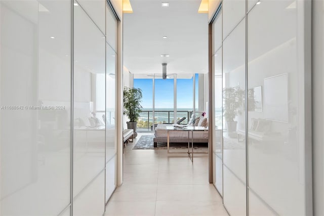 hall featuring light tile patterned floors, a water view, and floor to ceiling windows