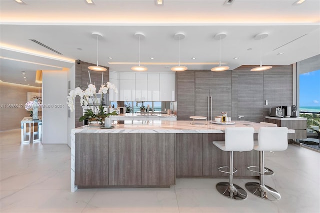 kitchen featuring light stone counters, a large island, pendant lighting, a breakfast bar, and white cabinets