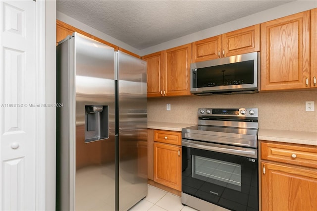 kitchen with a textured ceiling, light tile patterned floors, and stainless steel appliances