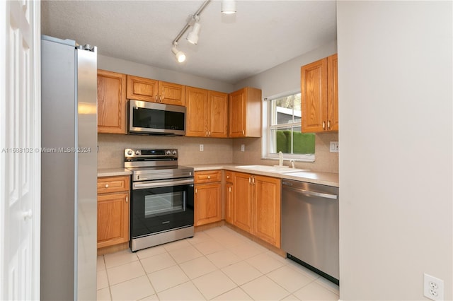 kitchen with light tile patterned flooring, sink, appliances with stainless steel finishes, rail lighting, and a textured ceiling