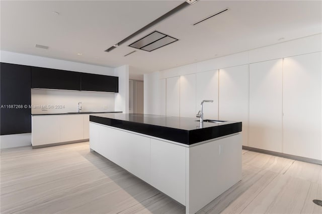 kitchen with white cabinetry, an island with sink, sink, and light hardwood / wood-style flooring