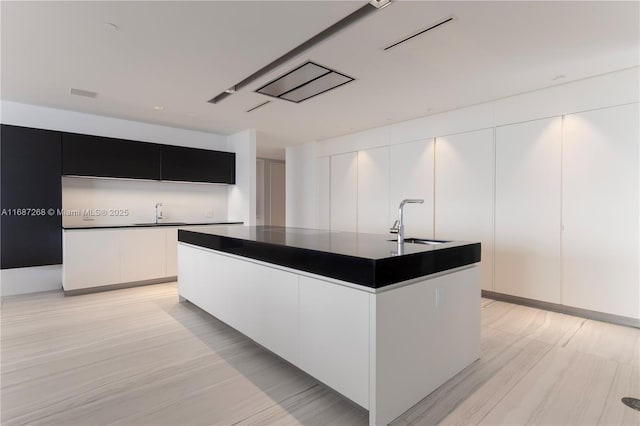 1000 Biscayne Blvd Unit 2702, Miami, FL 33132 - kitchen with dark countertops, modern cabinets, an island with sink, white cabinets, and light wood-type flooring