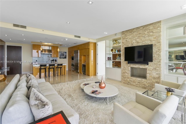 living room featuring built in features, light hardwood / wood-style flooring, sink, and a fireplace