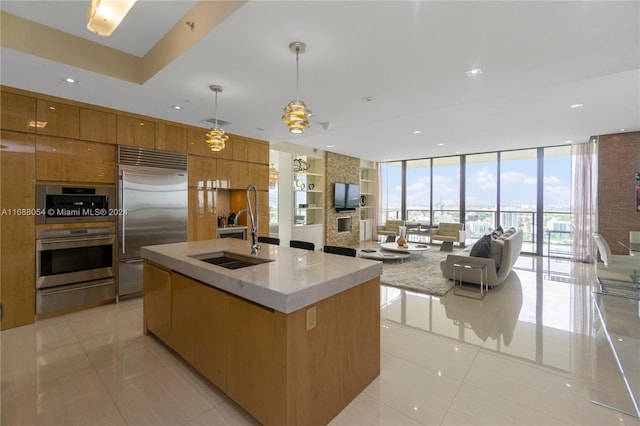 kitchen with stainless steel appliances, light tile patterned flooring, a center island with sink, sink, and hanging light fixtures