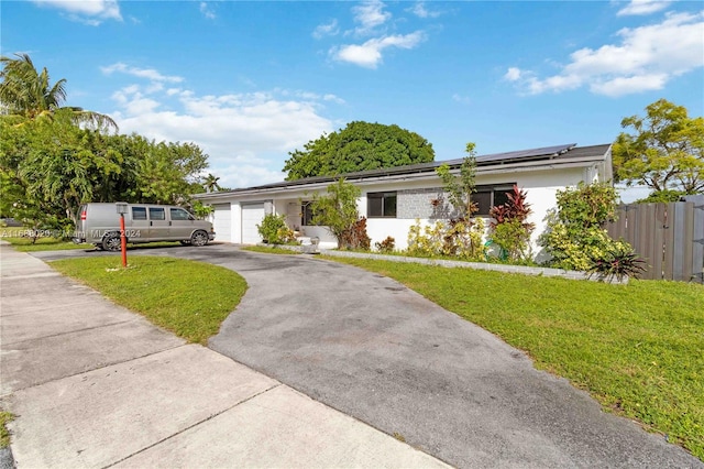 single story home featuring a garage, a front yard, and solar panels