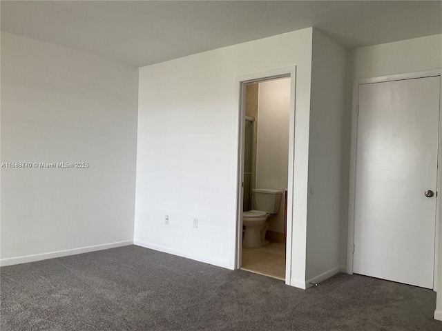 unfurnished bedroom featuring dark carpet and ensuite bath