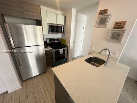 kitchen featuring sink, light wood-type flooring, an island with sink, appliances with stainless steel finishes, and white cabinetry