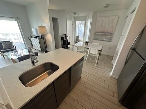 kitchen with dark brown cabinetry, sink, stainless steel dishwasher, and light wood-type flooring