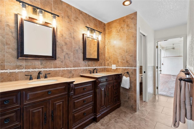 bathroom with vanity, tile patterned floors, ceiling fan, a textured ceiling, and tile walls