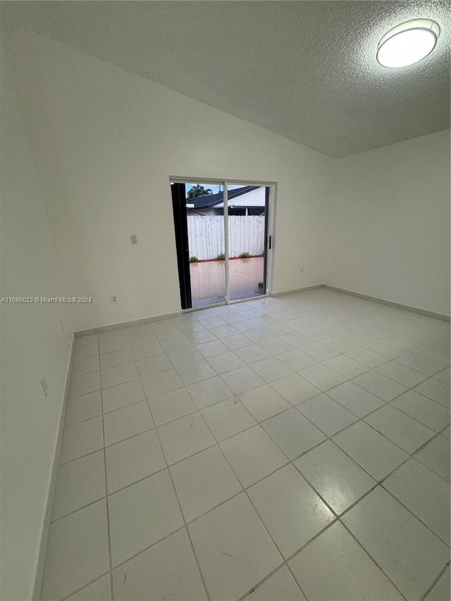 empty room with a textured ceiling, light tile patterned floors, and vaulted ceiling