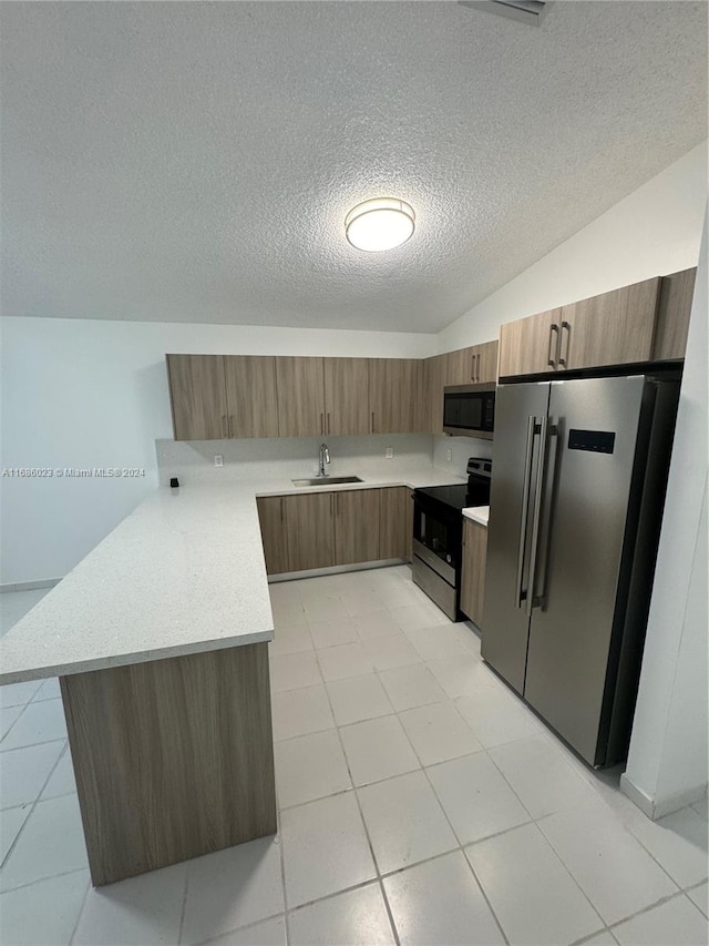 kitchen featuring lofted ceiling, kitchen peninsula, a textured ceiling, sink, and appliances with stainless steel finishes