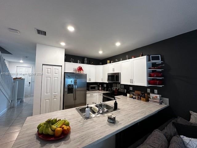 kitchen with stainless steel appliances, sink, kitchen peninsula, light tile patterned floors, and white cabinets