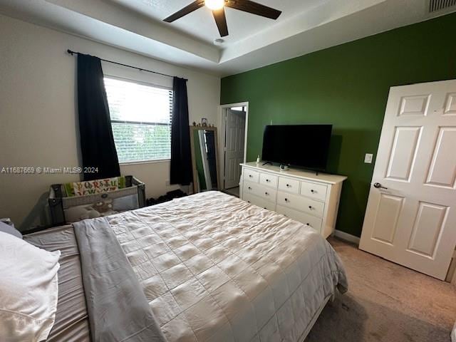 carpeted bedroom featuring a tray ceiling and ceiling fan