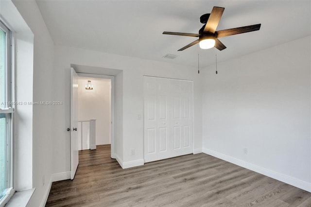 unfurnished bedroom featuring multiple windows, hardwood / wood-style floors, ceiling fan, and a closet