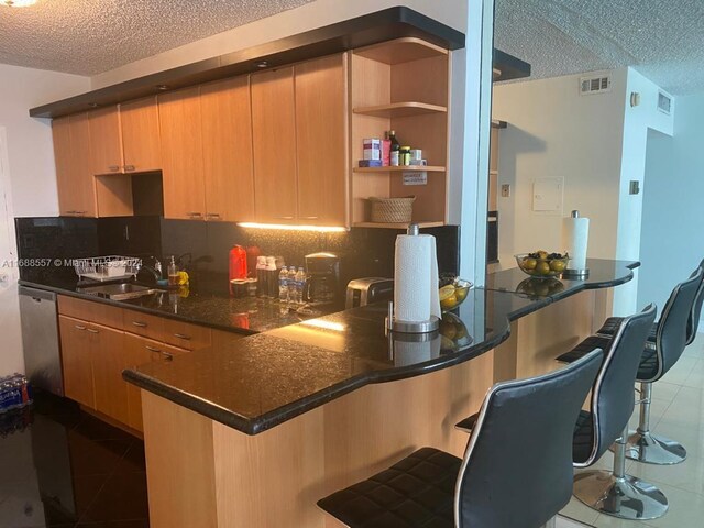 5401 Collins Ave Unit 412, Miami Beach, FL 33140 - kitchen with tile patterned floors, a textured ceiling, dishwasher, backsplash, and a breakfast bar