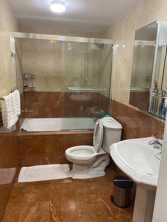 bathroom with toilet, bath / shower combo with glass door, and tile walls