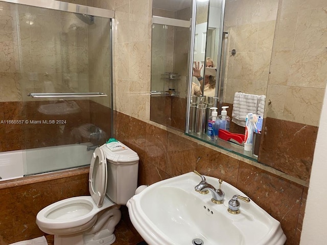 full bathroom with toilet, tile walls, sink, and shower / bath combination with glass door