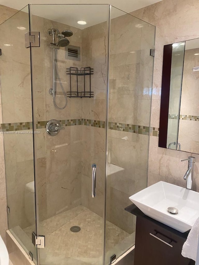 bathroom with a shower with door, vanity, and tile walls