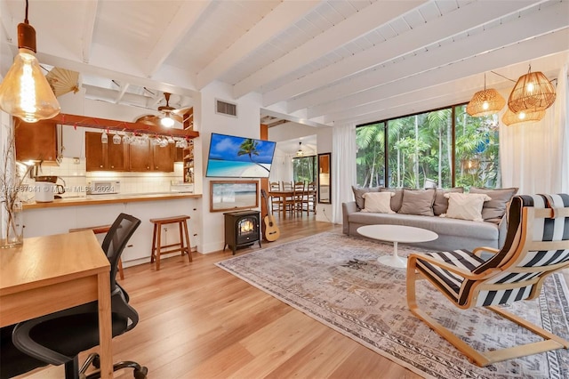 living room featuring beam ceiling, a wood stove, and light hardwood / wood-style flooring