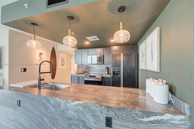 kitchen with tasteful backsplash, pendant lighting, appliances with stainless steel finishes, and sink