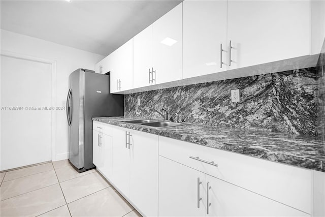 kitchen featuring dark stone counters, decorative backsplash, sink, light tile patterned floors, and white cabinetry