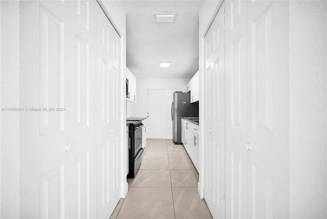 kitchen featuring light tile patterned flooring, black range with electric cooktop, white cabinetry, and stainless steel refrigerator