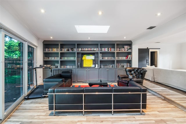 living room featuring a barn door, ornamental molding, light hardwood / wood-style flooring, and a skylight