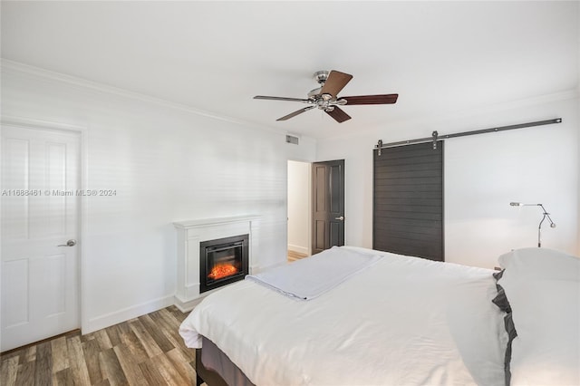 bedroom with ceiling fan, a barn door, wood-type flooring, and ornamental molding