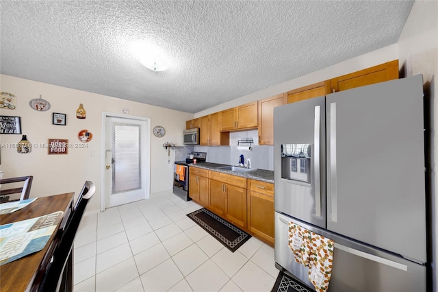 kitchen with a textured ceiling, sink, light tile patterned flooring, and stainless steel appliances