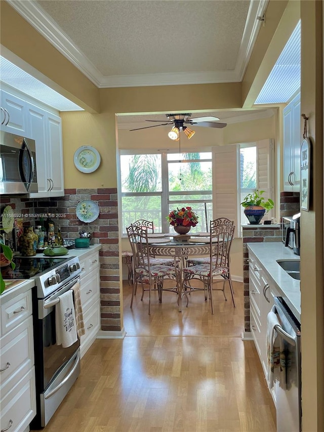 kitchen with crown molding, a textured ceiling, light wood-type flooring, appliances with stainless steel finishes, and white cabinets