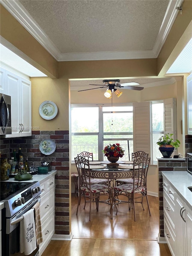 kitchen featuring white cabinets, stainless steel appliances, crown molding, a textured ceiling, and light hardwood / wood-style flooring