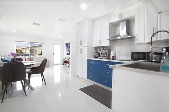 kitchen featuring light tile patterned flooring, backsplash, wall chimney range hood, blue cabinetry, and white cabinets