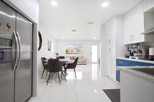 kitchen with stainless steel refrigerator with ice dispenser, white cabinetry, light tile patterned floors, and exhaust hood