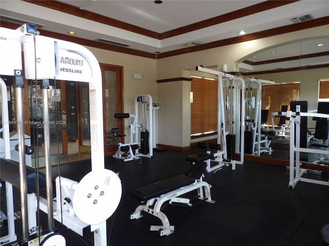 workout area with a raised ceiling and ornamental molding