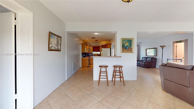 kitchen featuring a breakfast bar, light tile patterned floors, white refrigerator, and kitchen peninsula