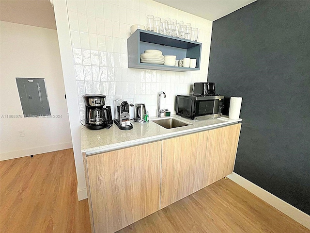 kitchen with sink, light brown cabinets, tasteful backsplash, electric panel, and light wood-type flooring