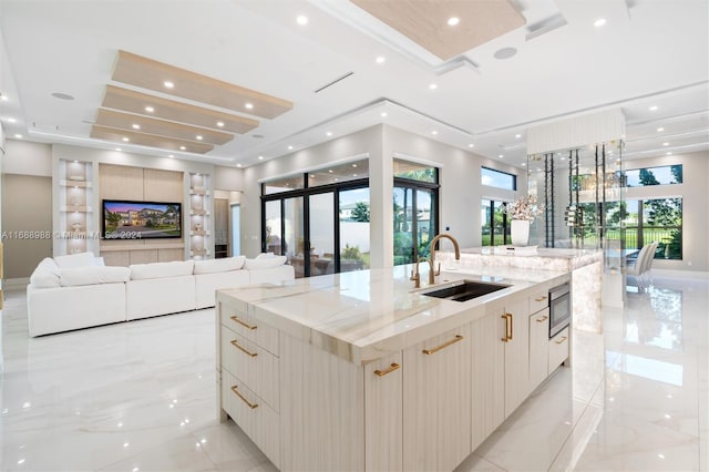 kitchen featuring light stone counters, stainless steel microwave, sink, a large island, and a tray ceiling